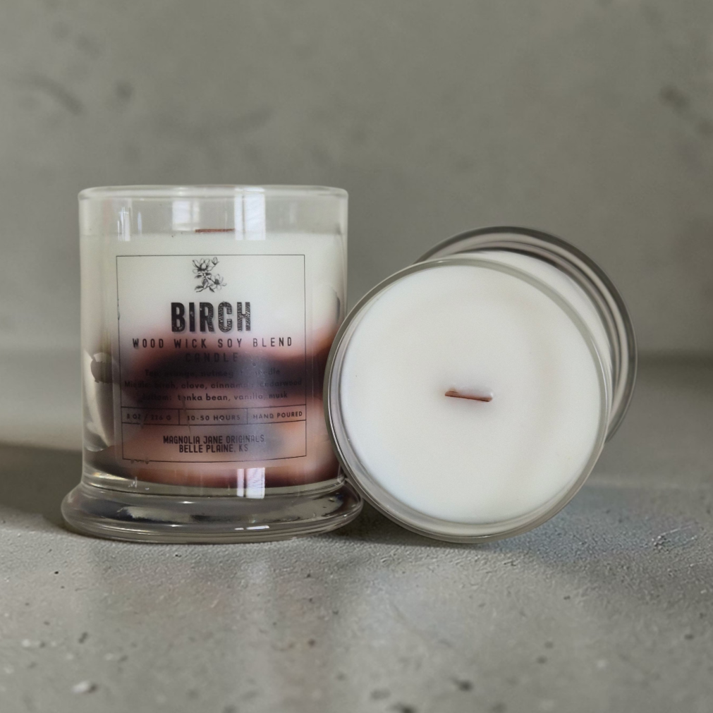 Birch is a wooden wick candle that is a creamy white color with a swirl design on the lower half of the candle in tans and browns
