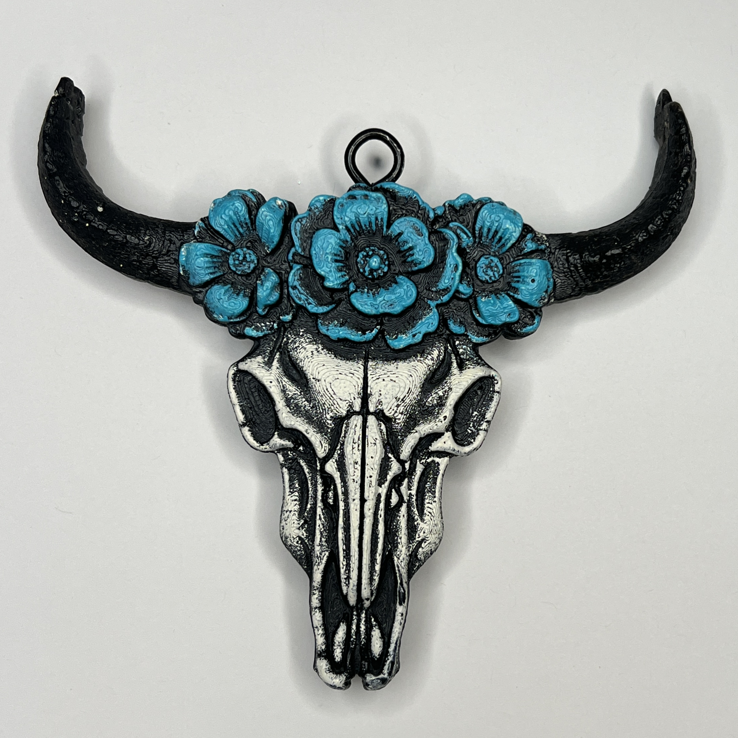 Decorative air freshener of a bull skull with blue flowers and black horns on a light gray background.