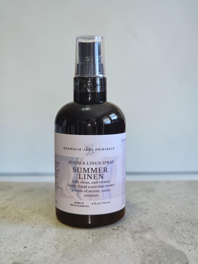 A fine mist room/linen spray in a black bottle with a white labe that has instructions and the description Soft, clean, and creamy fruity-floral scent that evokes a sense of serene, sunny comfort.