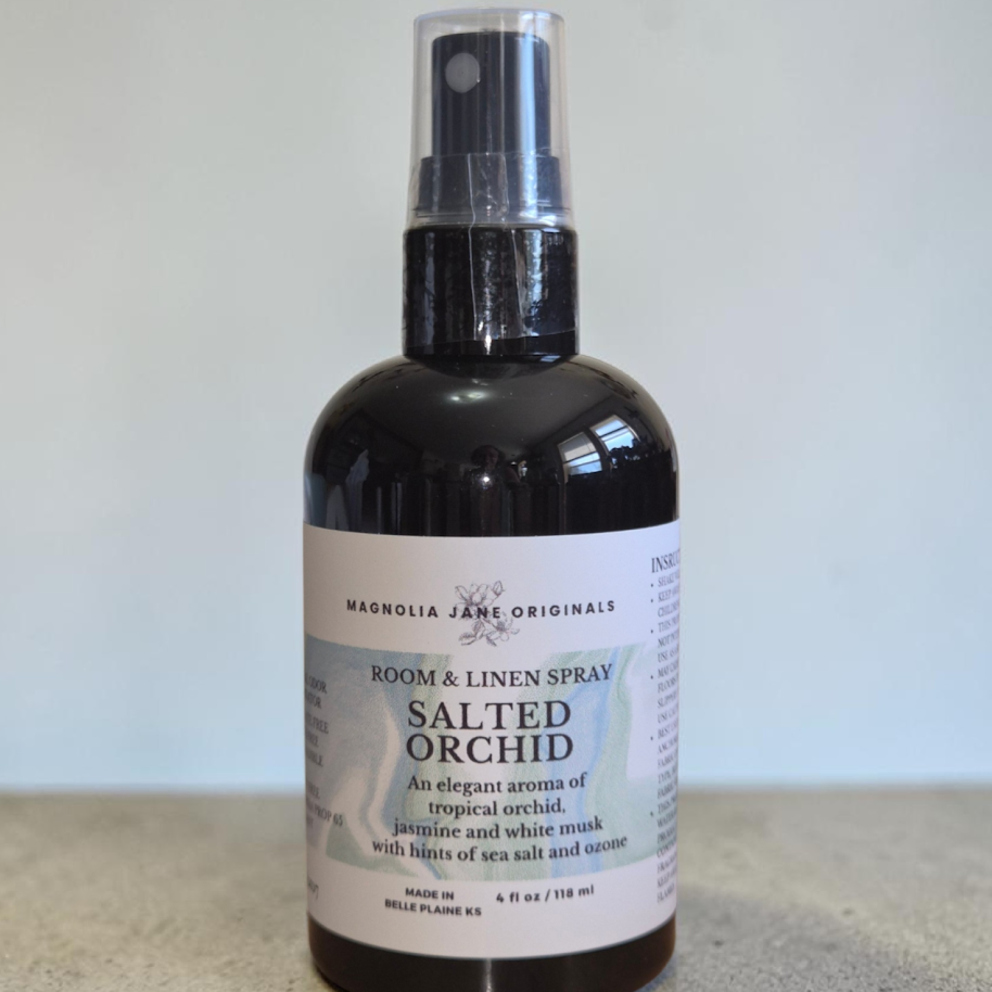 A fine mist room/linen spray in a black bottle with a white labe that has instructions and the description An elegant aroma of tropical orchids, jasmine, and white musk with hints of sea salt and ozone.