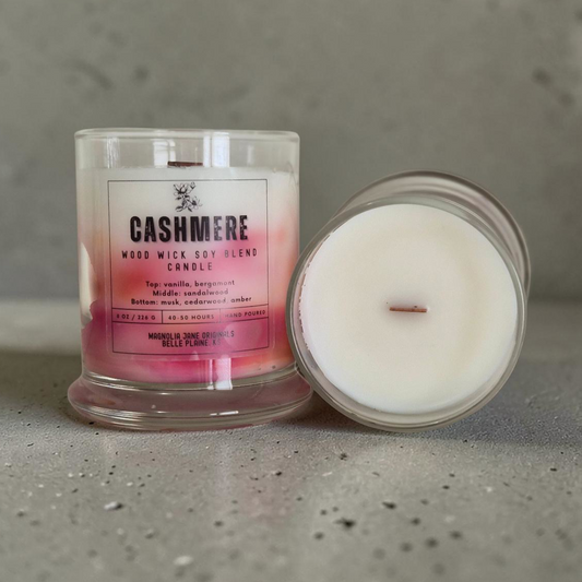 Cashmere is a wooden wick candle that is a creamy white color with a swirl design on the lower half of the candle in shades of pink and peach