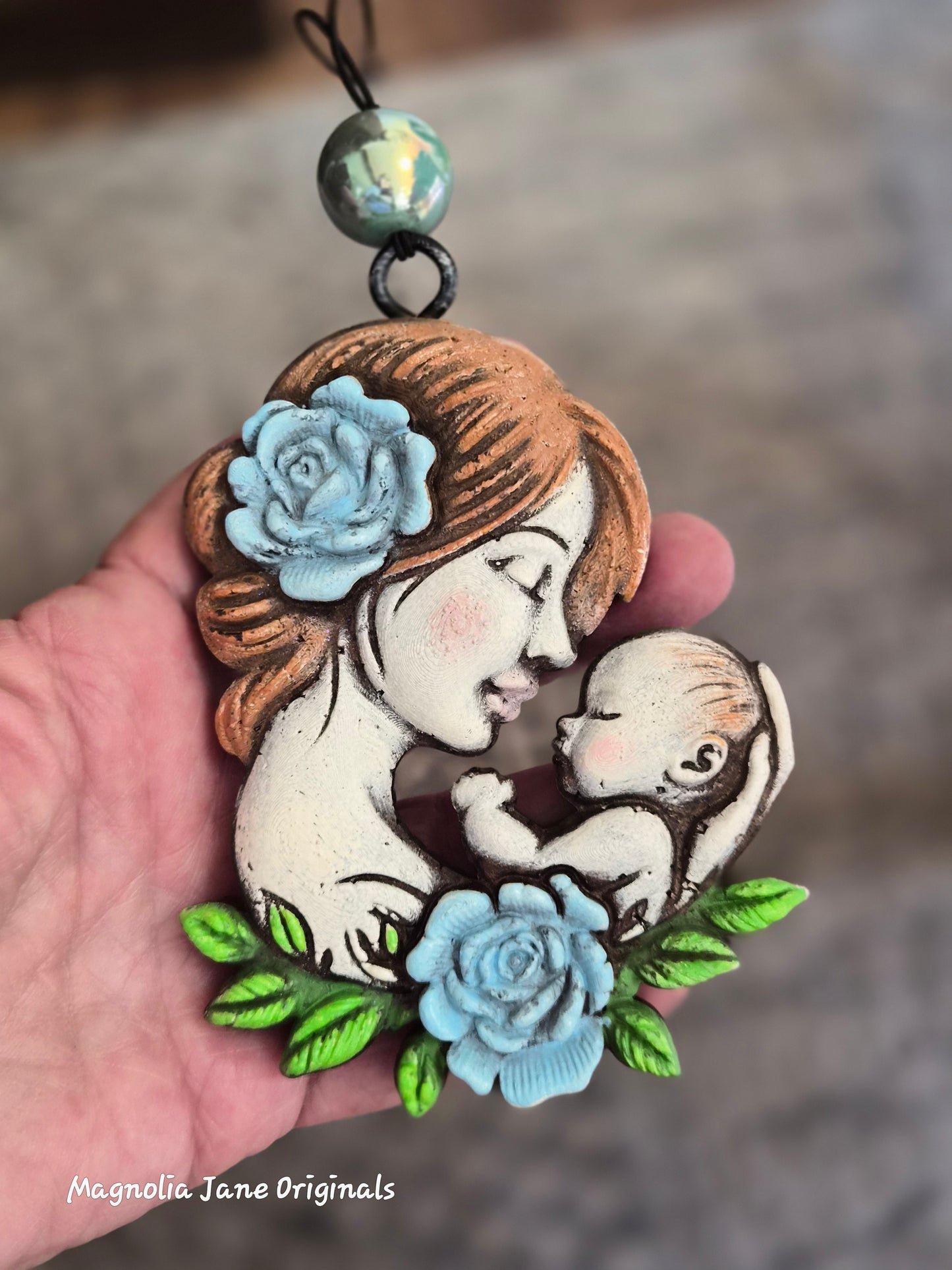 Mother & Baby  with light blue roses & green leaves air freshener for any type of vehicle held in a hand with a blurred background