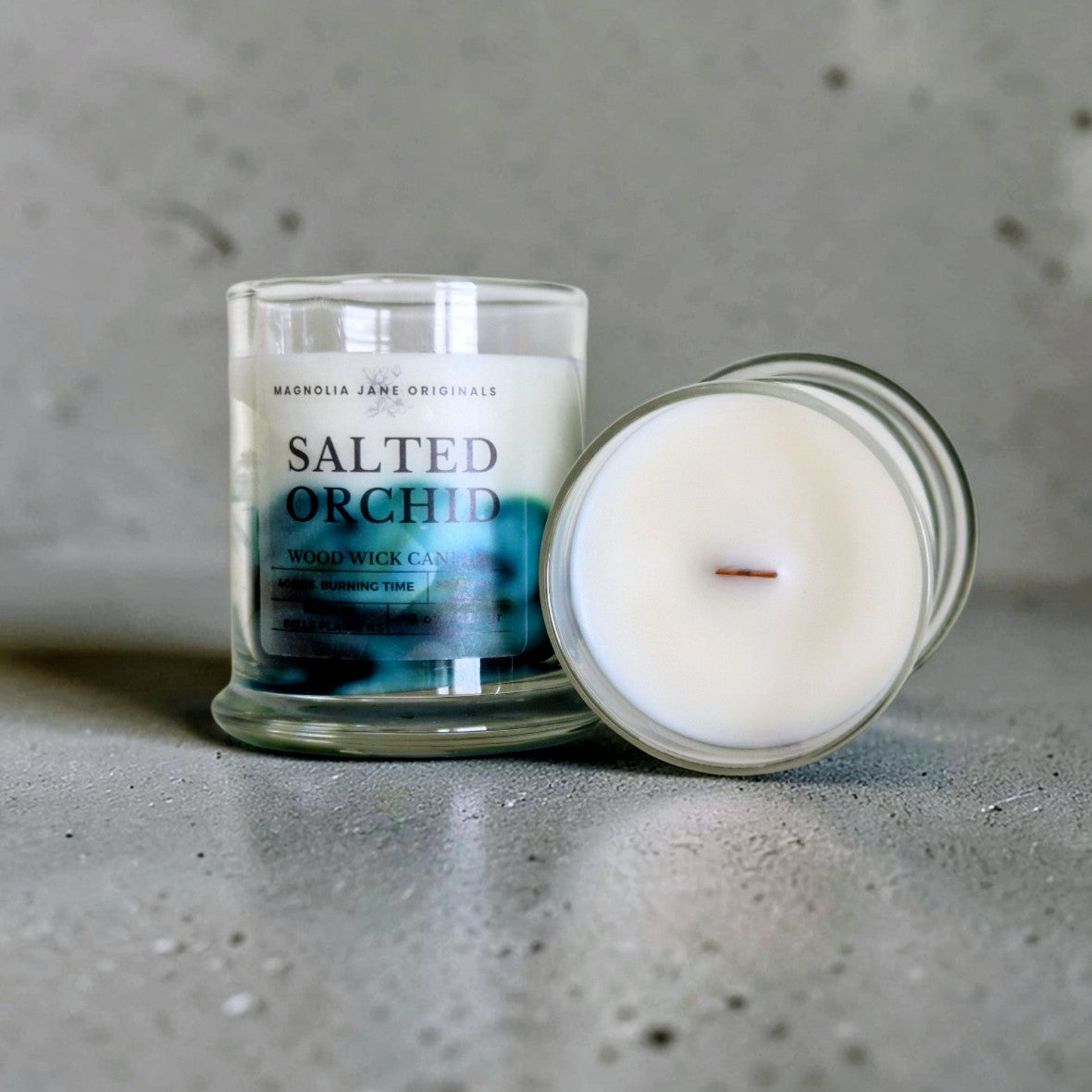 Salted Orchid is a wooden wick candle that is a creamy white color with a swirl design on the lower half of the candle in teal & green